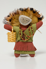 a small doll-like fetish with a headdress of feathers, beaded necklace, mask and dress made of leather.